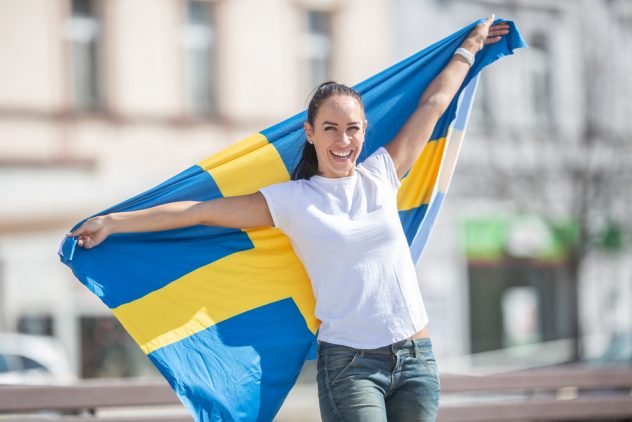 Smiling female fan holds Swedish flag on a street.